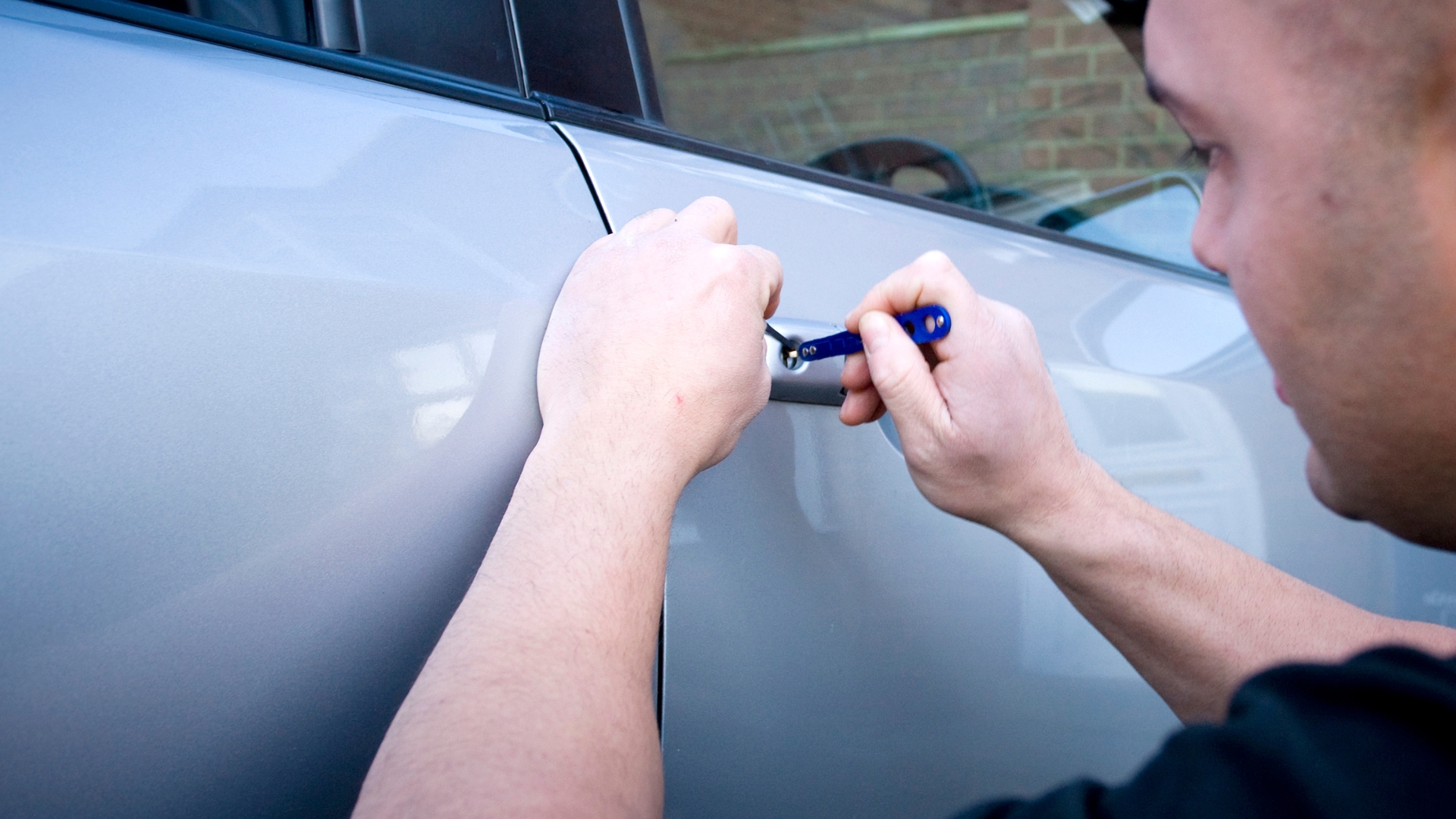 An auto locksmith uses a tool to unlock a car door, possibly due to broken car keys.