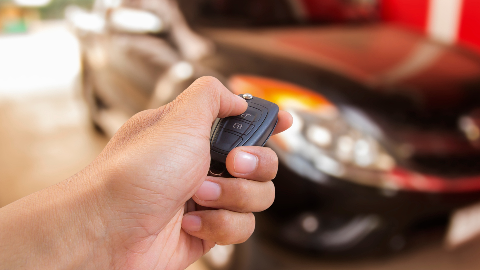 Hand holding a car key fob in front of a blurred vehicle, illustrating replacement fob cost in Sherman Oaks, CA.